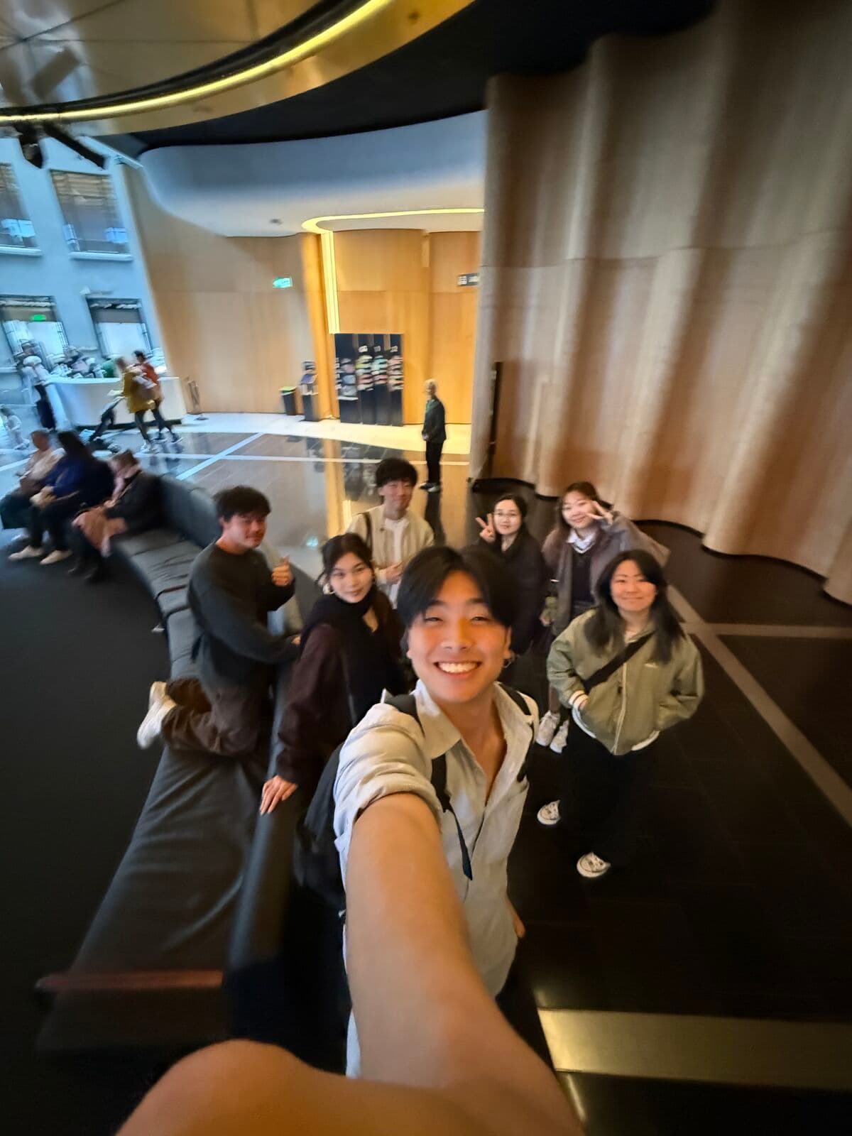 Eric taking a selfie with a group of friends in a lobby with curved wooden walls