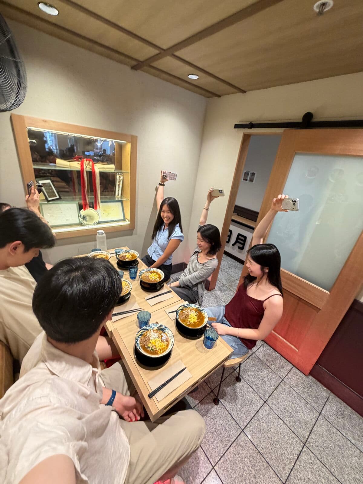 Eric and friends over bowls of noodles in a small dining room, three of them holding up their phones