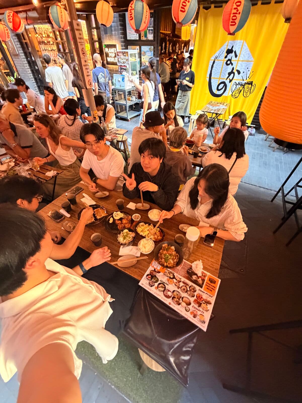 A crowded table of friends at an izakaya hung with paper lanterns