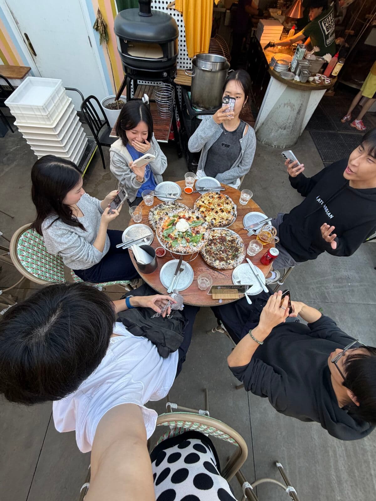 Friends around a table of pizzas and drinks on an outdoor terrace, seen from above