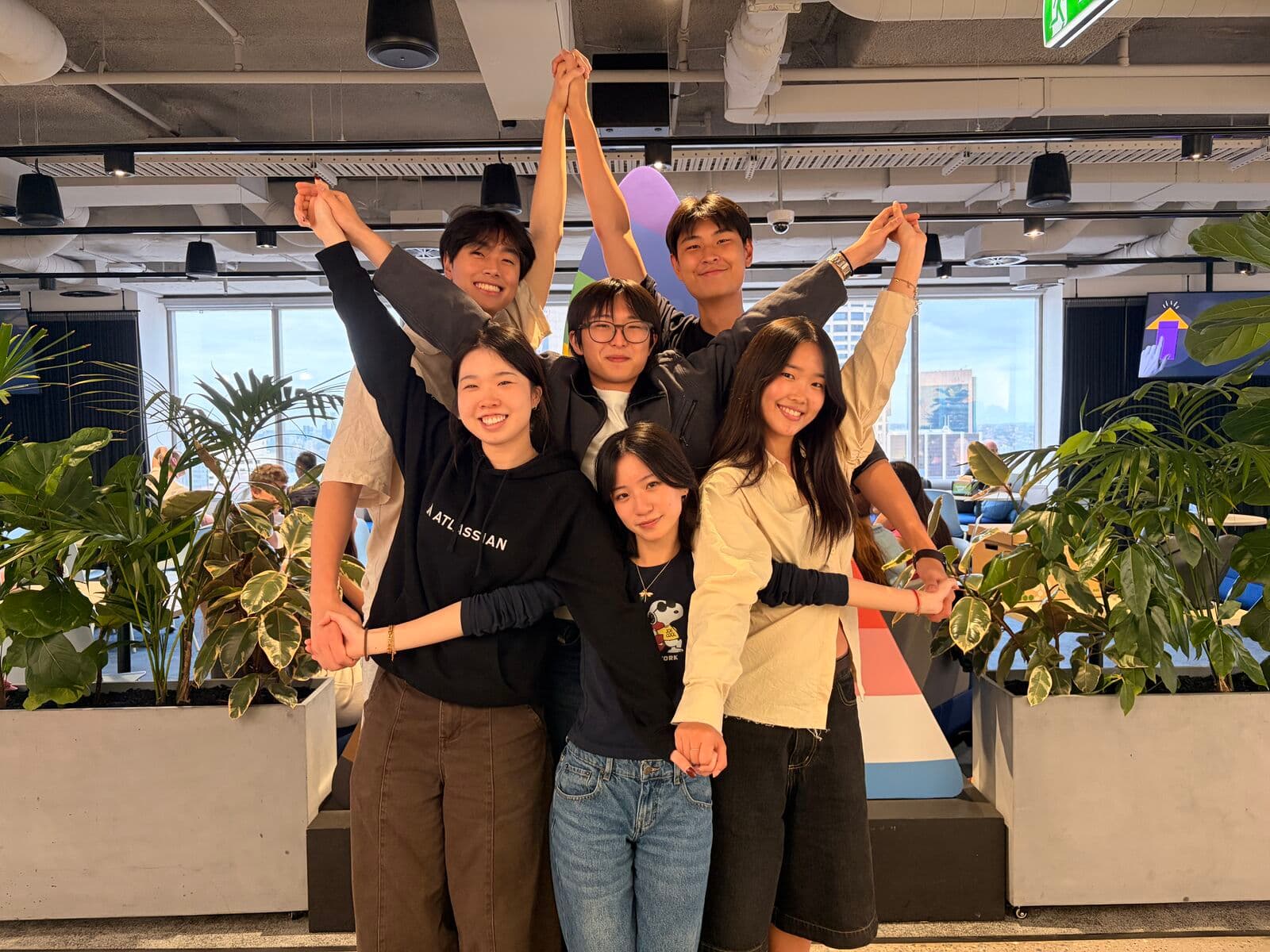 Eric and five friends posing arm in arm with their hands raised in an open-plan office