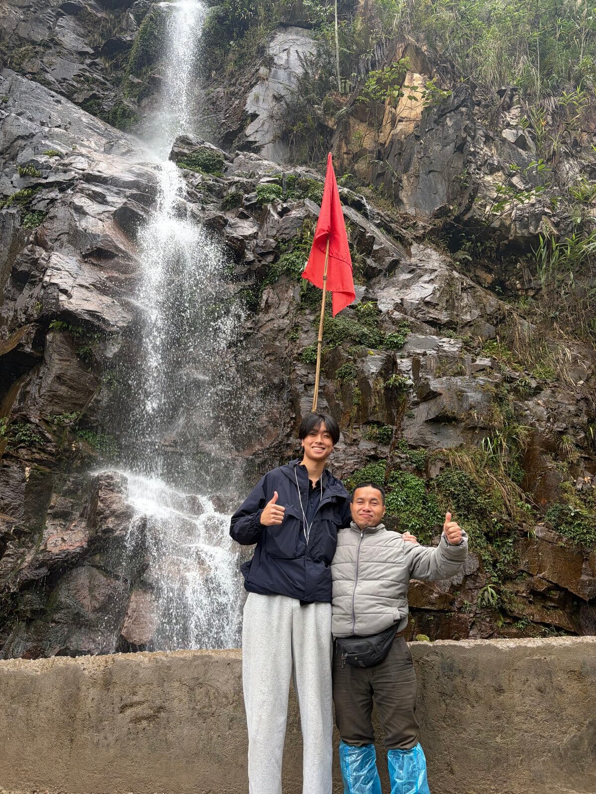 Eric and a man giving a thumbs up in front of a waterfall