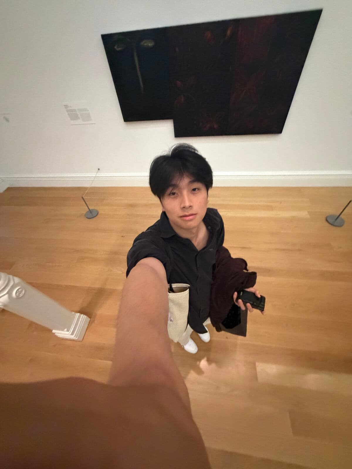 Eric taking a selfie alone in a gallery, under a large dark painting