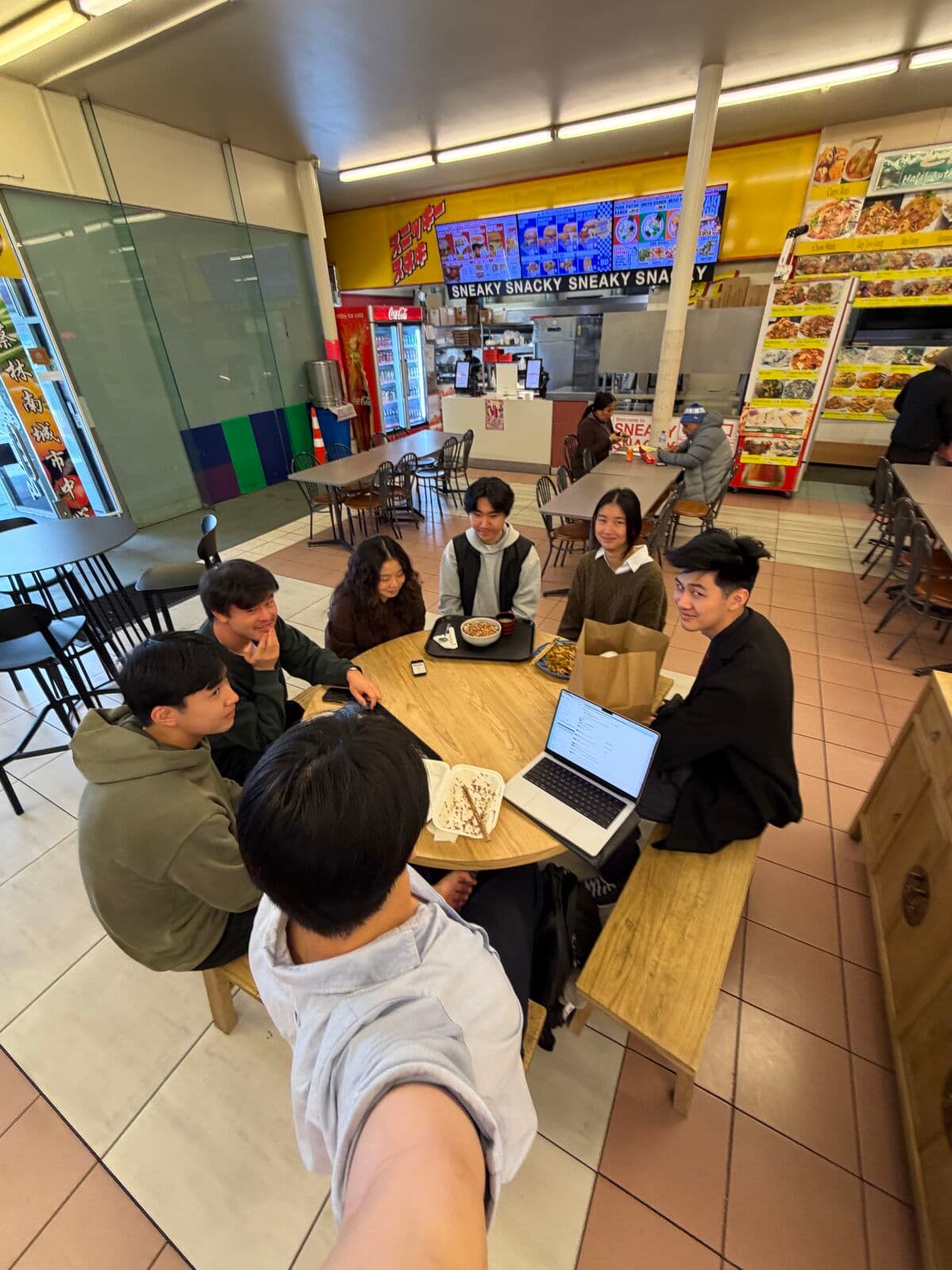 Eric and friends around a table with a laptop in a late-night takeaway shop