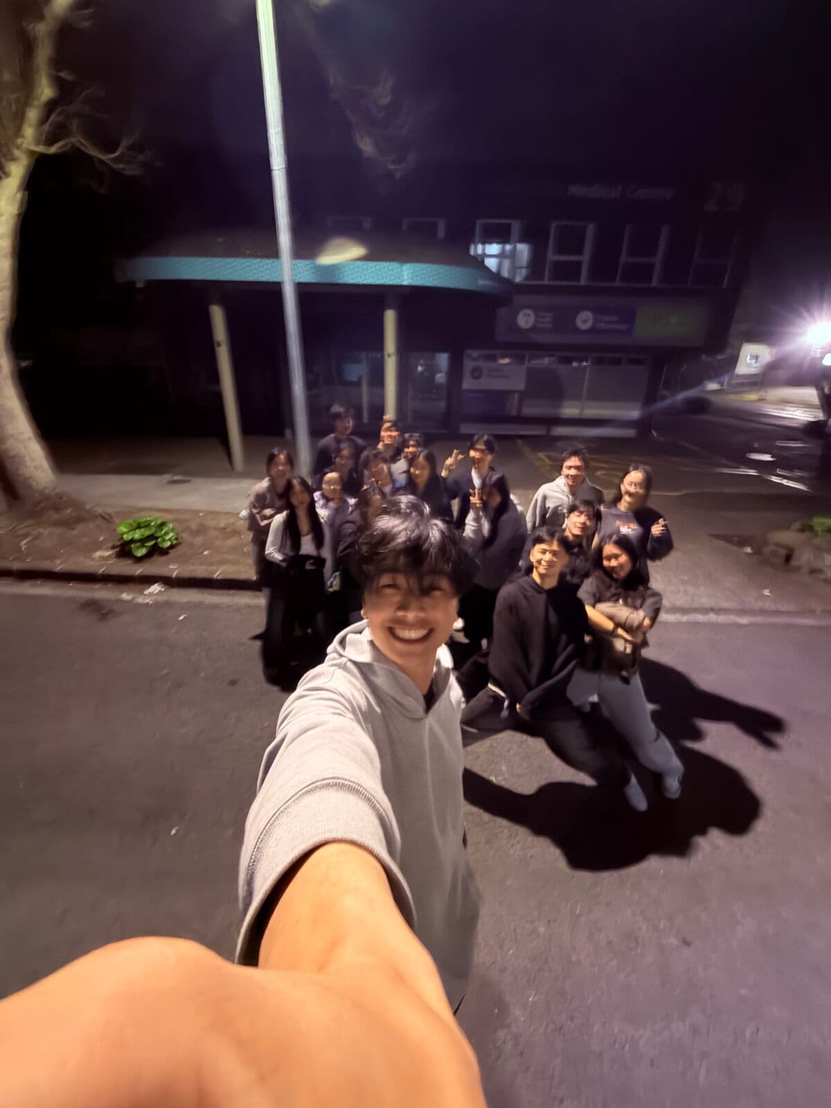 Eric taking a selfie on a dark street, a group of friends behind him